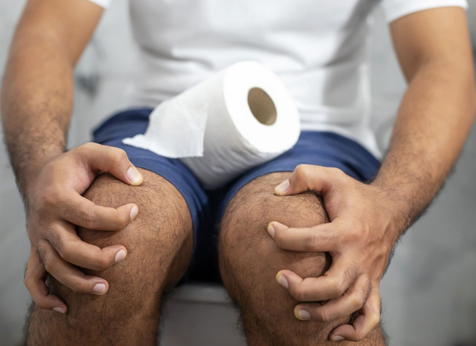 Man seated on a toilet with tissue paper placed on his thigh