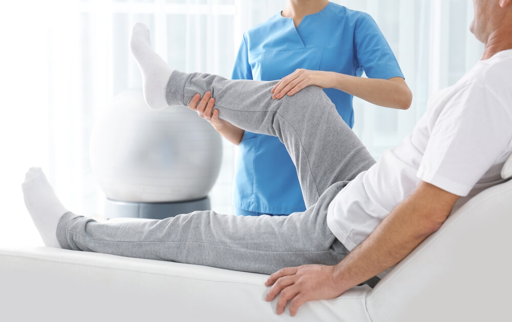 Gentle Physiotherapy Treatment: Therapist Providing Care to a Man in Semi-Reclined Position, Focusing on his Left Leg