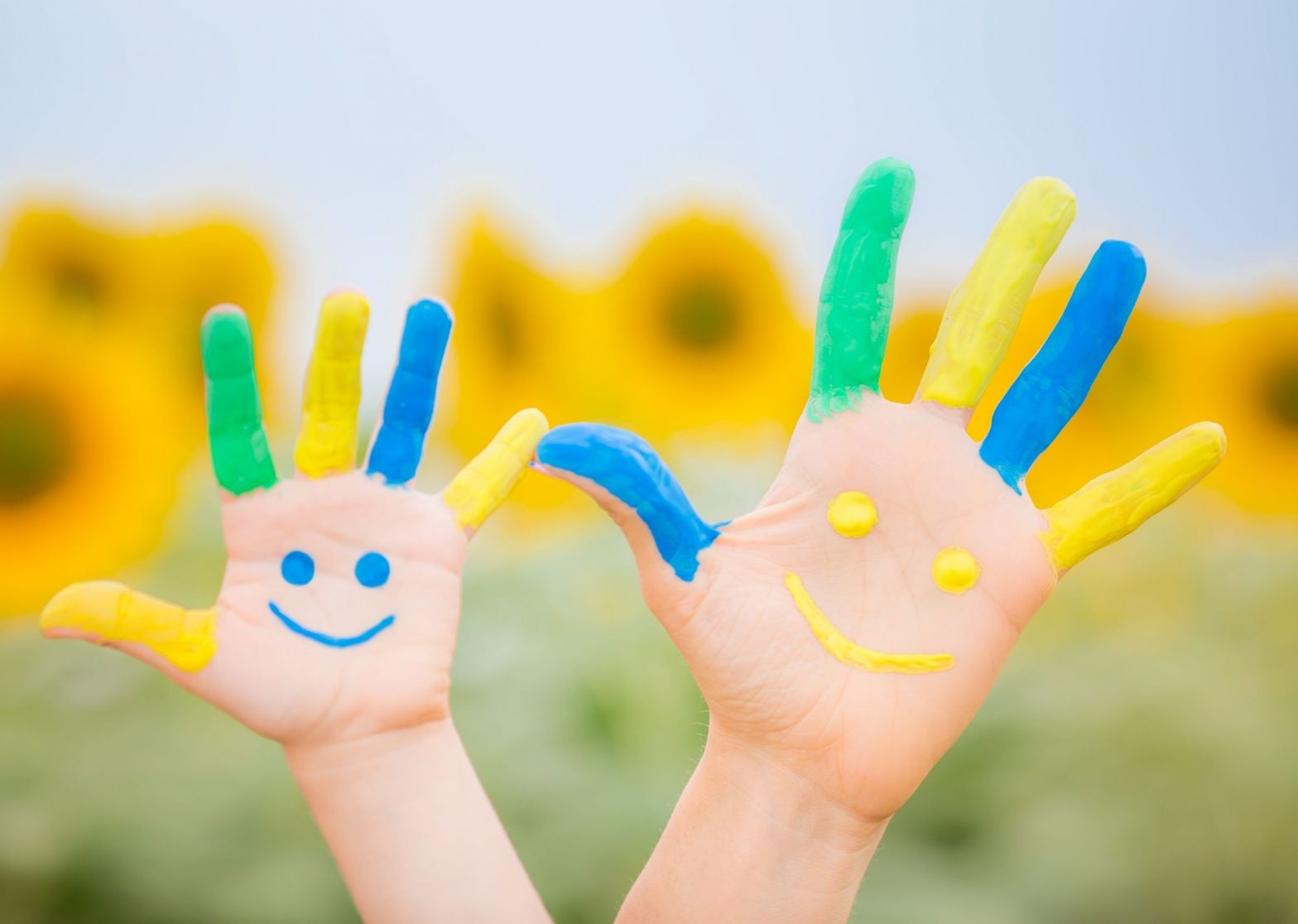 Two hands, one belonging to an adult and the other to a child, with painted fingers and a smiley face on the palm