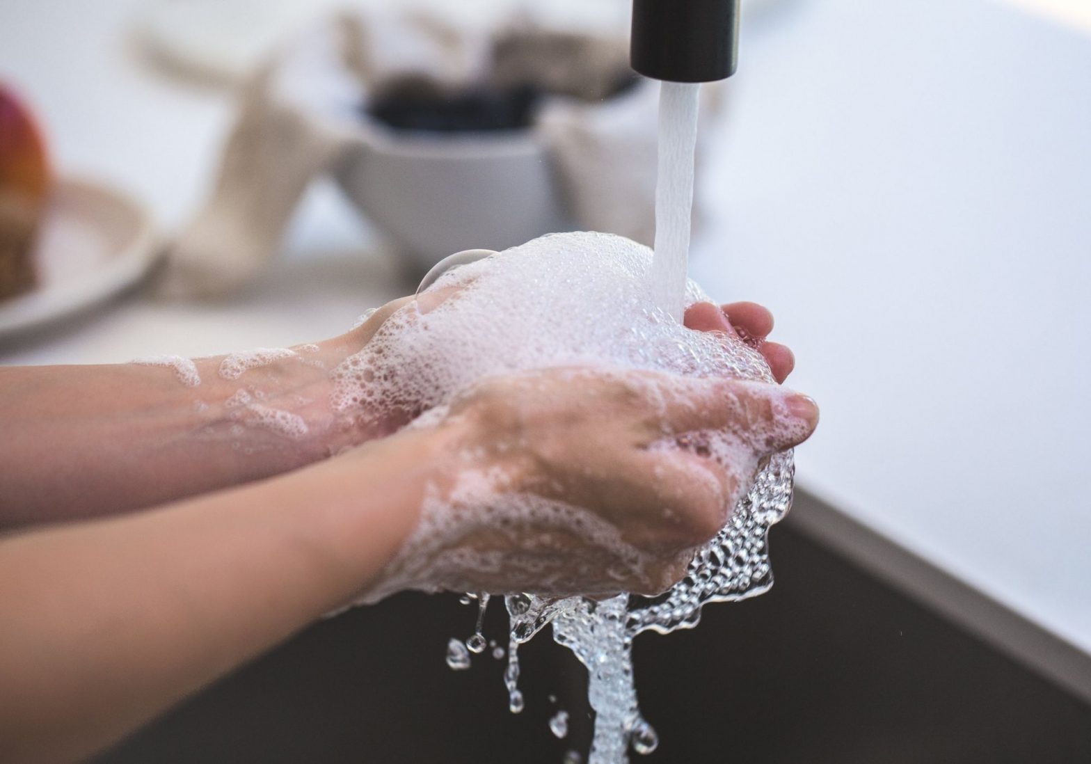 Hands covered in soapy bubbles under a running faucet