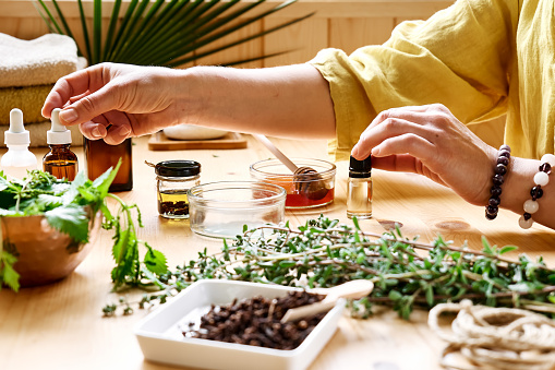 Herbs scattered on a table as a woman prepares medicinal herb mixture, picking up bottled medicine