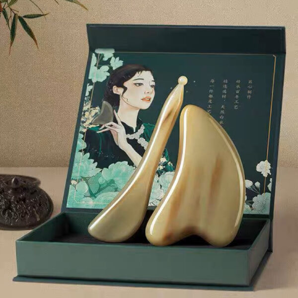 A set of facial gua sha tools neatly displayed inside a green box, positioned against a light brown background.